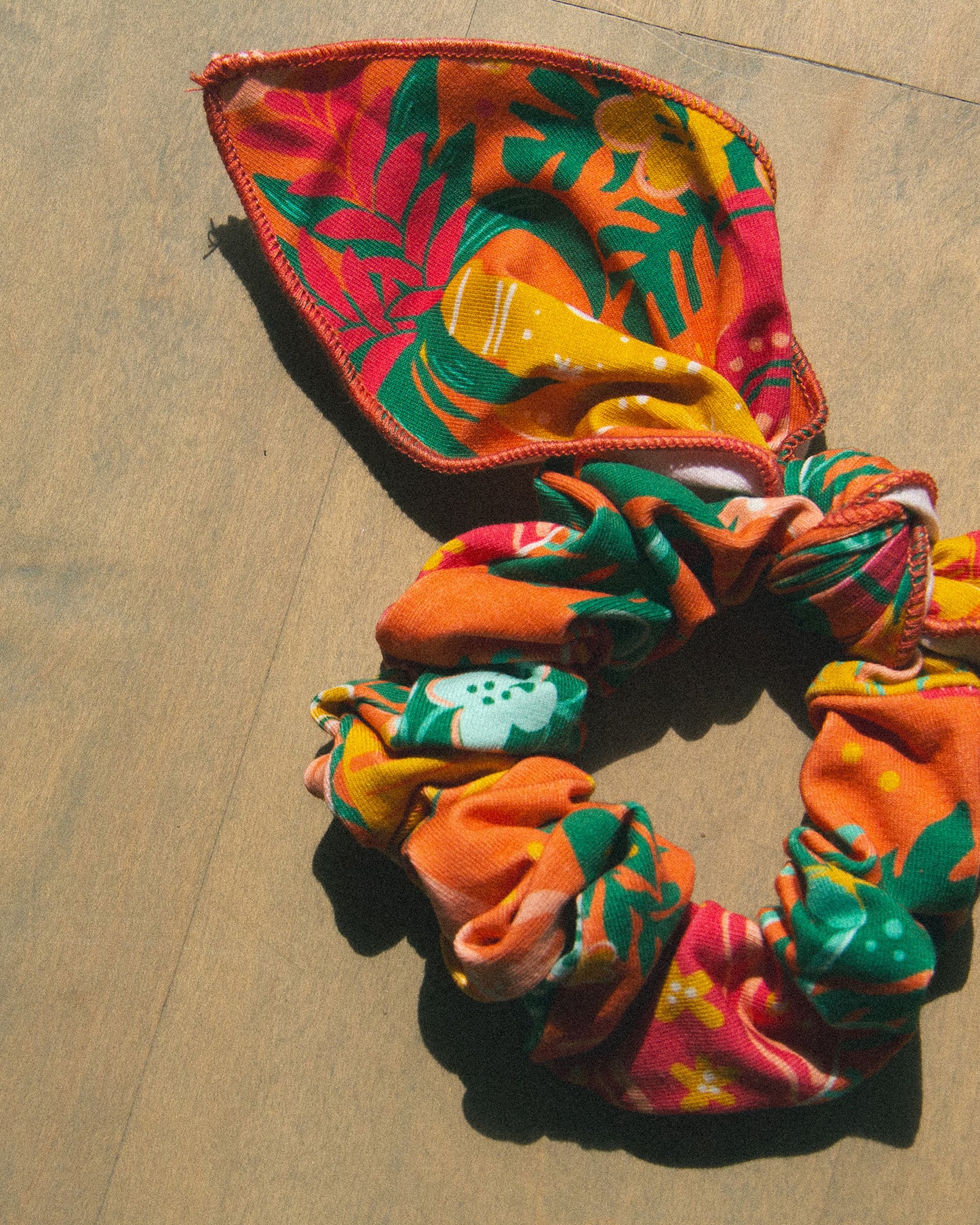An orange, yellow, and pink large scarf tie scrunchie with tropical leaves and palms. 
