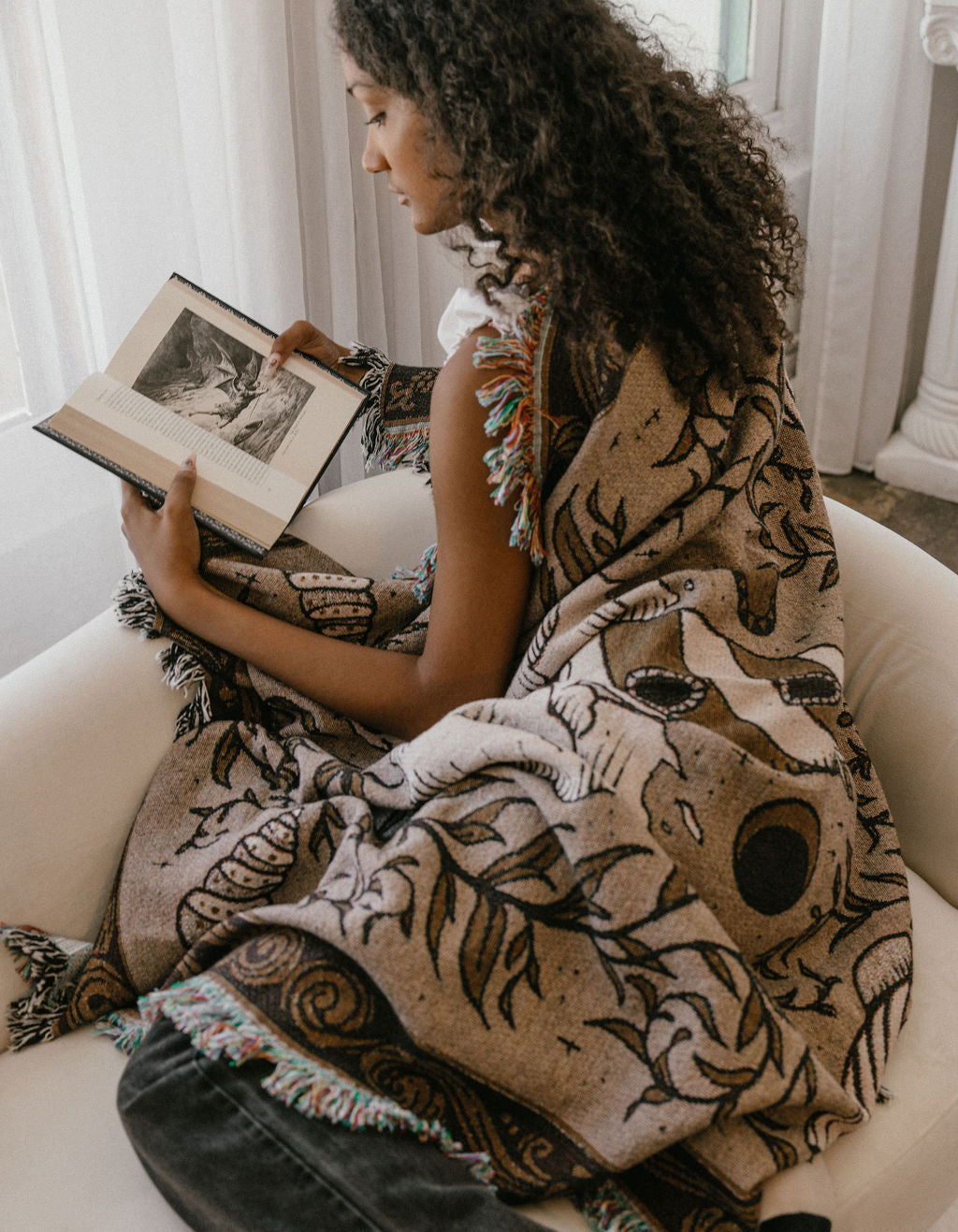 A woman wrapped in a cozy brown, cream, and beige woven blanket with a fringe. 
