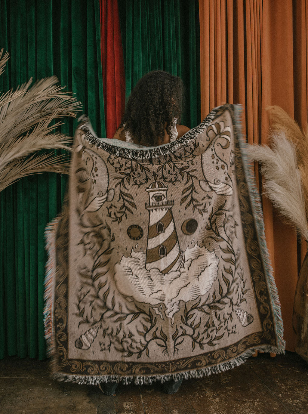A beautiful throw blanket with a lighthouse, whales, seashells, and other nautical imagery woven onto it in neutral tones of beige, white, and brown. 