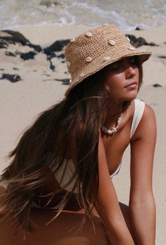 A tan crochet bucket hat with cowry shells woven on it for women's casual beachy style. 