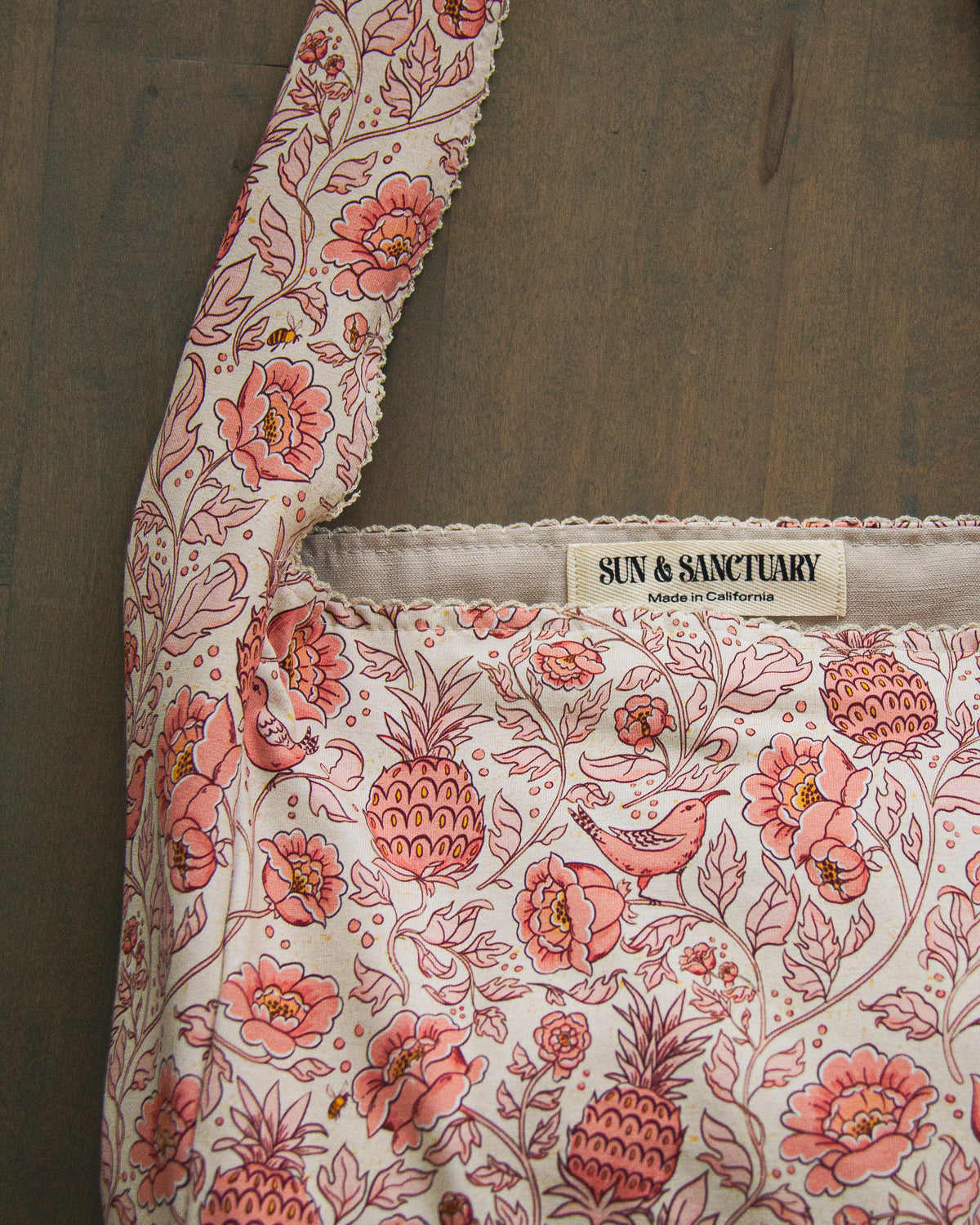 A slouchy hobo bag with lace fringe, printed with a pattern of flowers, pineapples, and tropical birds. 