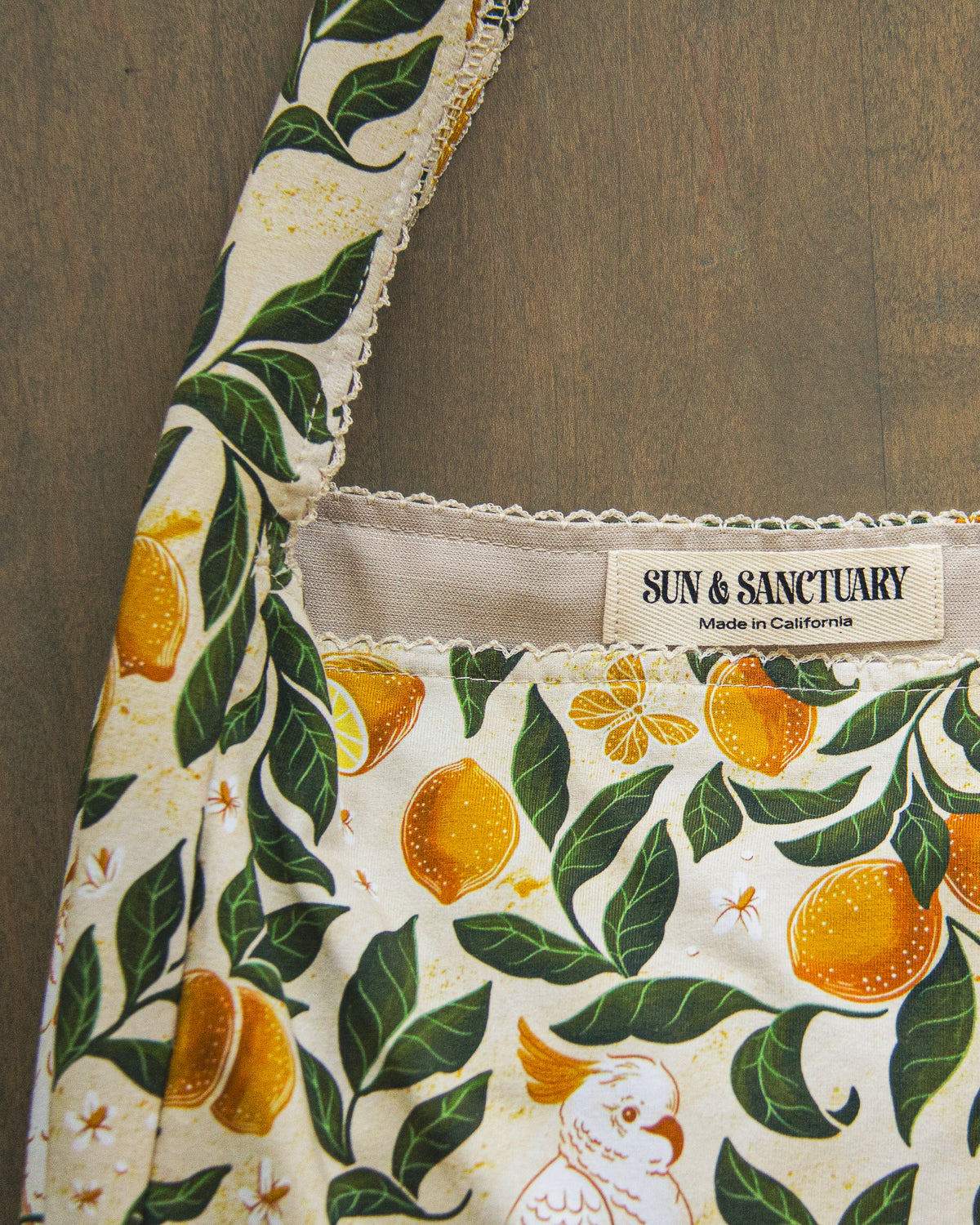 A close up on a boho fashion tote bag for women's casual style with lace trim, the Sun & Sanctuary logo, and a colorful lemon print. 